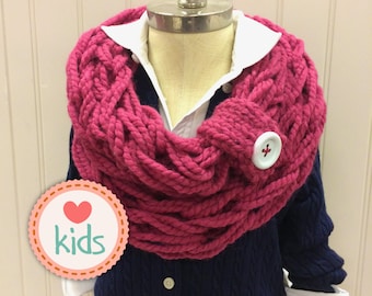 May include: A pink knitted infinity scarf with a white button. The scarf is worn on a mannequin wearing a navy blue cardigan and a white shirt. The image includes the text "I love kids".