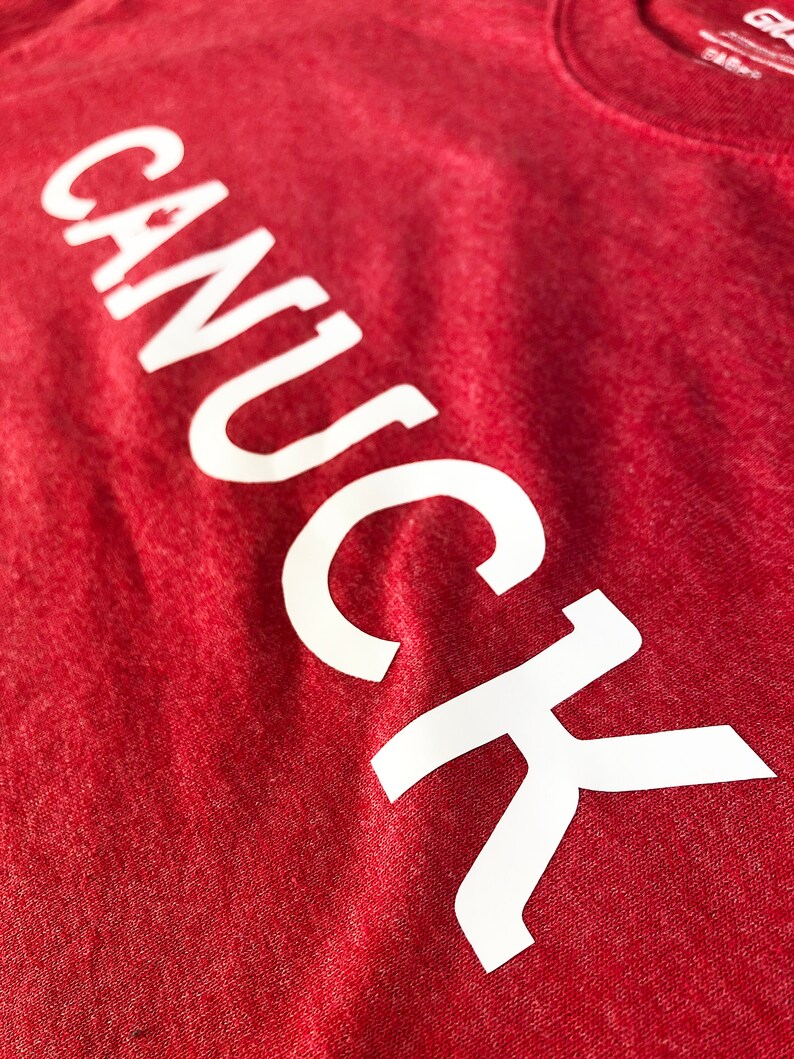 May include: Red t-shirt with the word "CANUCK" printed in white on the front.