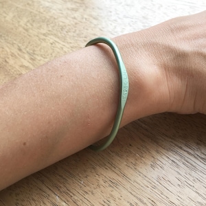 May include: A green metal bangle bracelet with the inscription "MINIMAL" on the inside.