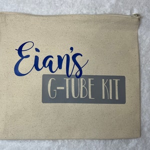 May include: A beige canvas zippered pouch with the text "Eian's G-TUBE KIT" in blue and gray lettering.