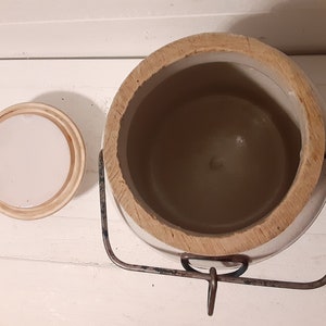 Puede incluir: Crock de cer&aacute;mica blanca con tapa de madera y asa de metal. El crock est&aacute; vac&iacute;o y la tapa est&aacute; quitada.