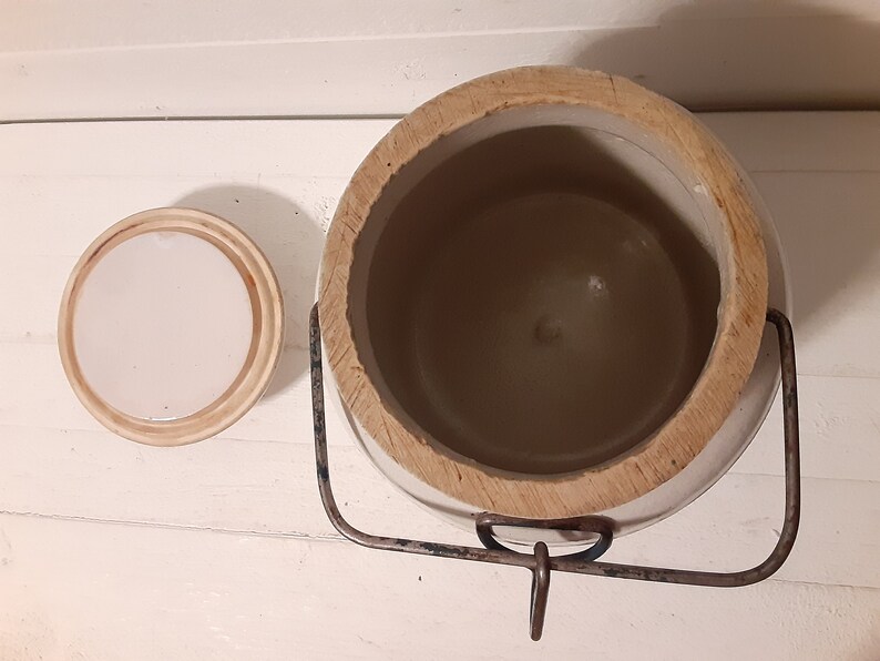 Puede incluir: Crock de cer&aacute;mica blanca con tapa de madera y asa de metal. El crock est&aacute; vac&iacute;o y la tapa est&aacute; quitada.