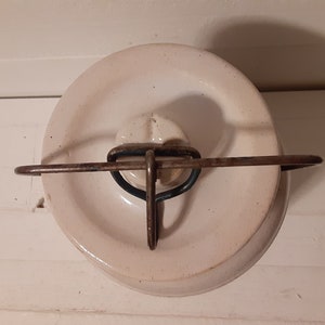 Puede incluir: Tarro de cer&aacute;mica blanco con tapa de metal y asa de alambre. La tapa tiene un pomo en relieve en el centro.