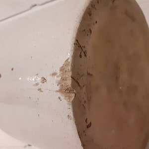 Puede incluir: Un tarro de cer&aacute;mica blanco con una grieta en el lateral. El tarro tiene un aspecto desgastado y envejecido.