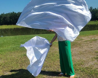 May include: Two large, white, rectangular fabric flags made of a lightweight, semi-sheer material. The flags are held in an extended, flowing position, creating large, billowing shapes that catch the air and display a smooth, satin-like texture.