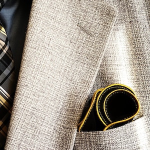 May include: A gray blazer with a black and white plaid tie. The blazer has a pocket with a black leather wallet.
