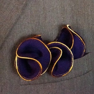Puede incluir: Una chaqueta de traje marr&oacute;n con una corbata amarilla y un pa&ntilde;uelo de bolsillo morado con ribete dorado.