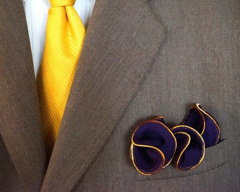 Puede incluir: Una chaqueta de traje marr&oacute;n con una corbata amarilla y un pa&ntilde;uelo de bolsillo morado con ribete dorado.