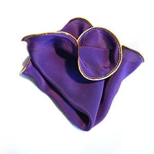 Puede incluir: Un pa&ntilde;uelo de bolsillo de seda morado con ribete dorado. El pa&ntilde;uelo est&aacute; doblado en forma triangular.