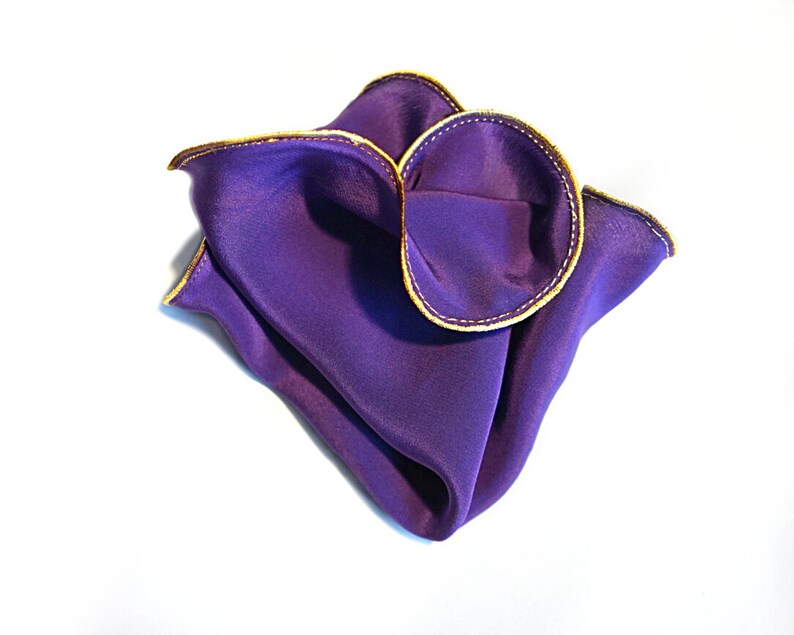 Puede incluir: Un pa&ntilde;uelo de bolsillo de seda morado con ribete dorado. El pa&ntilde;uelo est&aacute; doblado en forma triangular.
