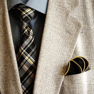 May include: A gray blazer with a black and yellow plaid tie and a black pocket square with a yellow border.