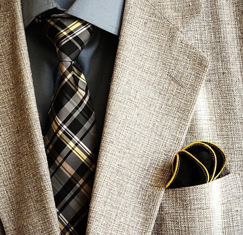 May include: A gray blazer with a black and yellow plaid tie and a black pocket square with a yellow border.