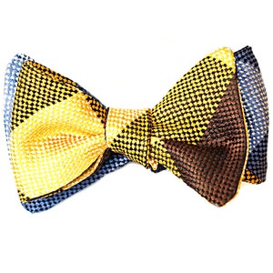 May include: A multi-colored bow tie with a repeating dot pattern. The bow tie features sections of yellow, brown, and blue fabric. The bow tie is a formal accessory.