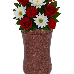 May include: A red granite urn with a floral arrangement of red roses, carnations, and white daisies. The urn has a wide base and a narrow neck. A small sign at the top reads "REMEMBER FOREVER UNIQUE URNS FOR ASHES".