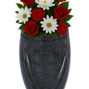 Puede incluir: Una urna negra moteada con un arreglo floral de rosas rojas, claveles y margaritas blancas. La urna tiene un diseño curvo y una etiqueta dorada que dice "REMEMBER FOREVER UNIQUE URNS FOR ASHES."