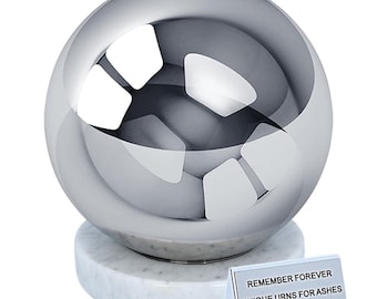 May include: A silver sphere urn with a white marble base. The urn is sitting on a white surface. The text on the card reads "Remember Forever Unique Urns for Ashes".