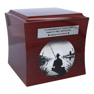 May include: A dark red wooden cremation urn with a silver plaque that reads "In Loving Memory of Timothy Smith August 12.1982-April 26.2024 Always in Our Hearts". The urn features a silver circular image of a person fishing on a lake.