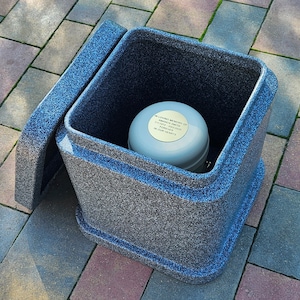 May include: A grey concrete urn with a lid. The urn has a gold plaque with the text "In loving memory of Amanda Smith 2/18/1983 - 3/20/2023 Forever in our hearts".