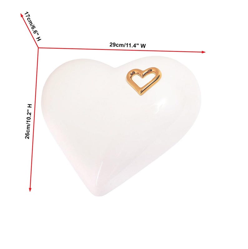 May include: A white heart-shaped decorative object, 11.4 inches wide, 10.2 inches high, and 6.6 inches deep, with a gold heart-shaped accent. The glossy surface reflects light, highlighting the smooth curves of the heart.