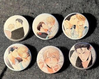 May include: Six round pinback buttons with illustrations of male figures in various romantic poses. The artwork features soft colors and detailed facial expressions, set against a light background. The buttons are arranged on a textured, dark surface.