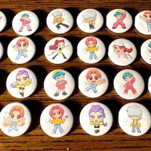 May include: A collection of 25 white, round buttons with colorful cartoon character illustrations. The characters are depicted in various poses and outfits, with a range of hair colors and styles. The buttons are arranged on a wooden surface.