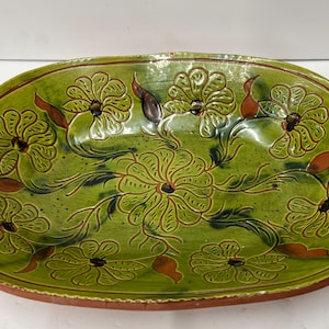 May include: An oval ceramic serving dish featuring a vibrant green glazed interior with embossed floral patterns. The design includes a central flower surrounded by smaller blossoms and leaves in shades of brown and dark green, with a terracotta rim.