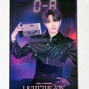 Peut inclure: Carte promotionnelle avec une personne tenant une radio vintage. Le texte "D-A" et "LIGHT THE WAY" sont visibles. L'arrière-plan est un dégradé de violet et de rouge. La carte est pour le concert ATEEZ VR.