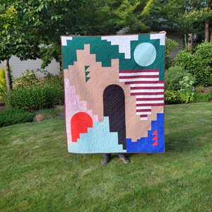 May include: A colorful geometric quilt with a green, brown, blue, red, white, and pink design. The quilt is made of different fabrics and has a patchwork style.