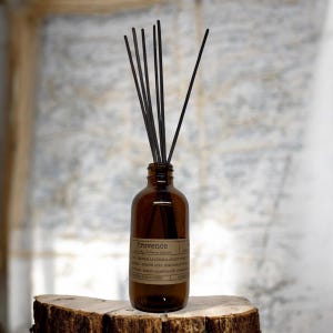 May include: A brown glass diffuser bottle with black reeds. The bottle has a label that reads "Provence" and lists ingredients. The diffuser sits on a wooden surface, with a blurred background.