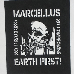 Puede incluir: Parche de tela negra con texto y gráficos blancos. El texto dice "MARCELLUS NO FRACKING NO COMPROMISE EARTH FIRST!". Un gráfico de calavera está en el centro, con una estructura en su boca.