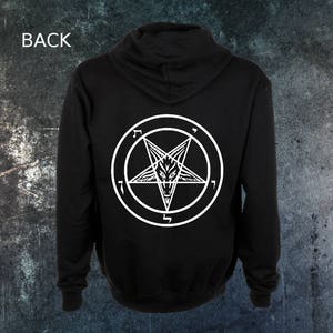 Könnte beinhalten: Schwarzer Kapuzenpullover mit einem weißen Pentagramm und einem Ziegenkopf darin. Das Pentagramm ist von einem Kreis mit fünf umgekehrten '7' umgeben.