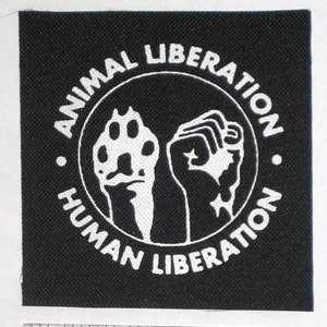 May include: Black fabric patch with white text and graphic. The text reads "Animal Liberation Human Liberation" in a circle around a paw print and a fist.