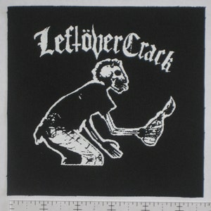 May include: Black and white patch with the text "Leftover Crack" in a gothic font. A skeleton figure holding a torch is in the center of the patch.
