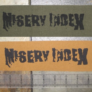May include: Two fabric patches with the text "MISERY INDEX" printed in black on a green and a brown background.
