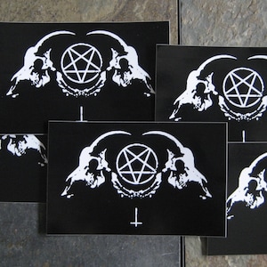 Könnte beinhalten: Fünf schwarze und weiße Aufkleber mit einem Pentagramm und zwei Schädeln. Das Pentagramm ist weiß und die Schädel sind weiß mit schwarzen Details. Die Aufkleber befinden sich auf einem grauen Hintergrund.