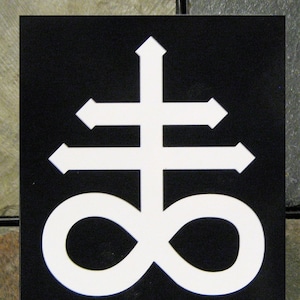 Könnte beinhalten: Ein weißes Symbol auf schwarzem Hintergrund. Das Symbol ist ein Kreuz mit einem Unendlichkeitszeichen am unteren Ende. Das Symbol wird oft mit dem Okkulten in Verbindung gebracht.