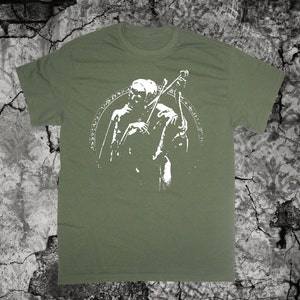 May include: A green t-shirt with a white graphic of a hooded figure holding a musical instrument. The figure is surrounded by a circle of symbols.