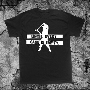 Pode incluir: Camiseta preta com uma silhueta branca de uma pessoa segurando um taco de beisebol e o texto "UNTIL EVERY CAGE IS EMPTY."