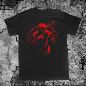 May include: Black t-shirt with a red graphic of a hooded figure playing a string instrument. The figure is surrounded by a circle of text.