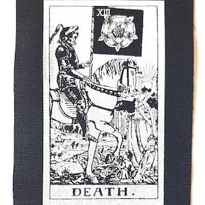 Könnte beinhalten: Schwarz-weißer Aufnäher mit der Illustration der Tarotkarte Tod. Das Bild zeigt eine skelettartige Figur auf einem Pferd, die eine Flagge mit einem Rosenemblem hält. Das Wort "DEATH" ist unten aufgedruckt.