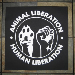Peut inclure: Patch noir et blanc avec un cercle contenant un poing levé et une empreinte de patte. Le texte autour du cercle est "Animal Liberation Human Liberation."
