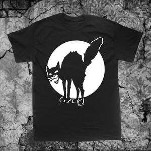 May include: Black t-shirt with a white graphic of a black cat in a circle. The cat is facing left and has its mouth open.