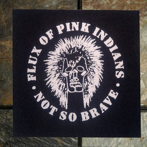 May include: A black fabric patch with white text and a white graphic of a skull wearing a headdress. The text reads "Flux of Pink Indians - Not So Brave".