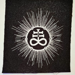 Peut inclure: Un patch en tissu noir avec un symbole blanc d'une croix avec un symbole d'infini à l'intérieur d'un cercle entouré d'un rayonnement solaire.