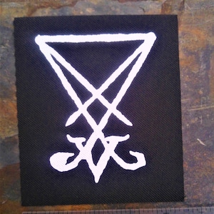 May include: White embroidered patch on a black fabric background. The patch features a white inverted pentagram with a white symbol inside.