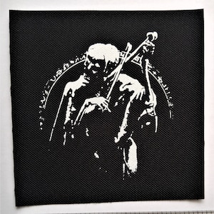 Könnte beinhalten: Schwarz-weiß-Patch mit einer skelettartigen Figur, die Cello spielt. Die Figur ist von einem Kreis mit Text umgeben.