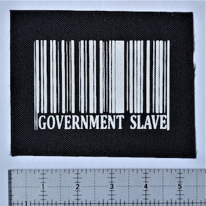 Puede incluir: Parche de tela negro con un código de barras blanco y el texto "GOVERNMENT SLAVE" impreso debajo.