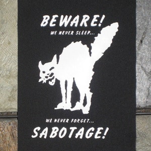 May include: Black and white patch with a white cat silhouette and the text "BEWARE! WE NEVER SLEEP... WE NEVER FORGET... SABOTAGE!"