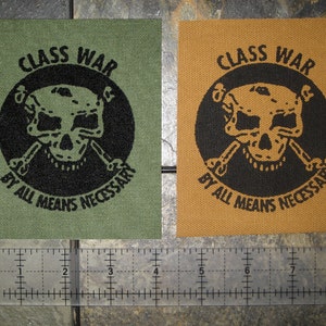 May include: Two fabric patches with a skull and crossbones design. The patches are green and brown with black text that reads "Class War By All Means Necessary".