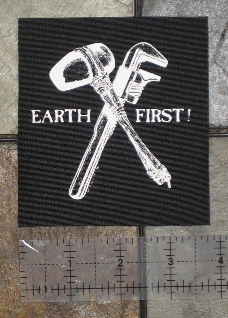 May include: Black patch with a white image of a crossed hammer and wrench. The text "EARTH FIRST!" is printed below the tools.